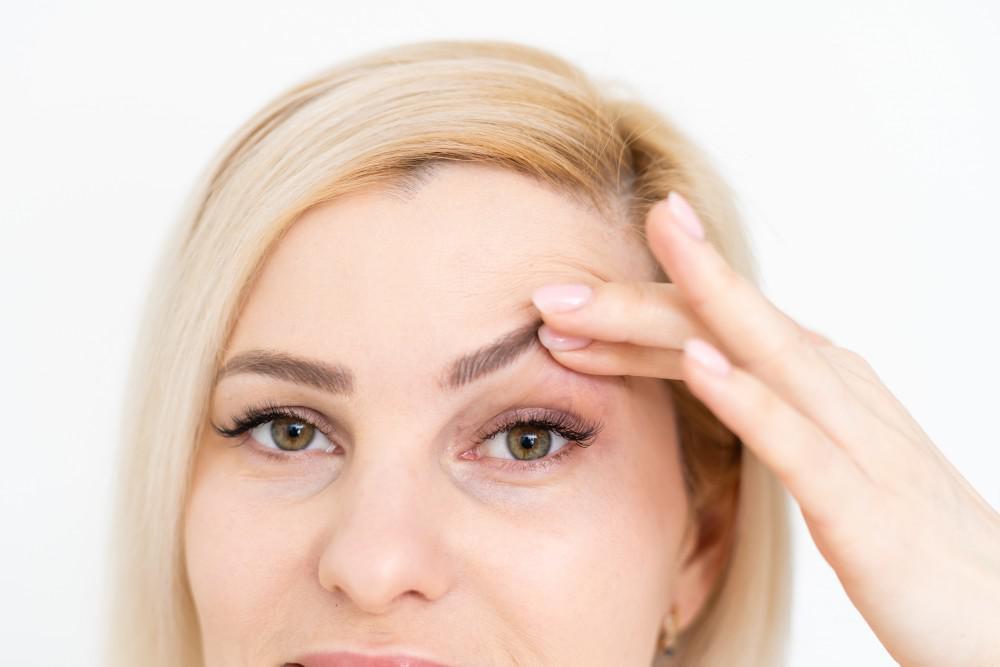 blonde hair lady holding up her eyelid with her finger