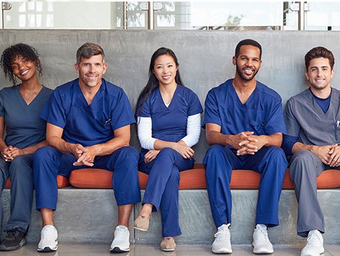 diverse group of doctors smiling and sitting on a bench