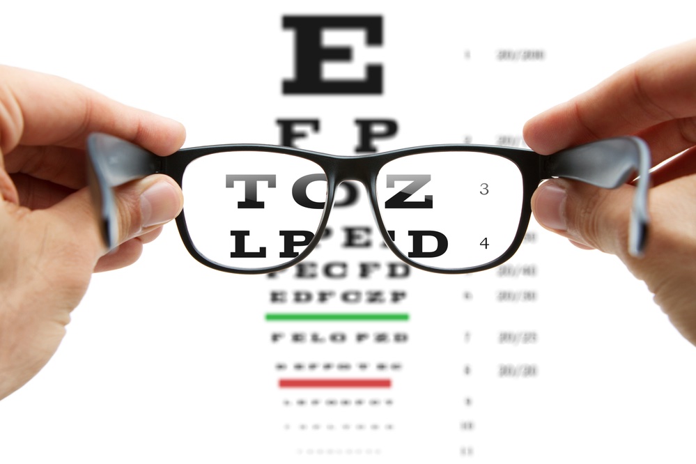 person holding eye glasses in front of an eye exam chart