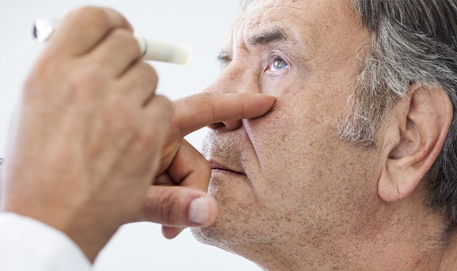 elder man getting a flashlight shinned in his eye during an eye exam by a doctor
