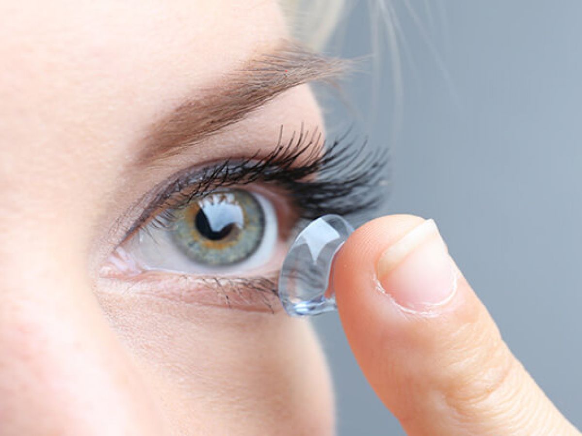 woman with long eyelashes putting in a contact lens