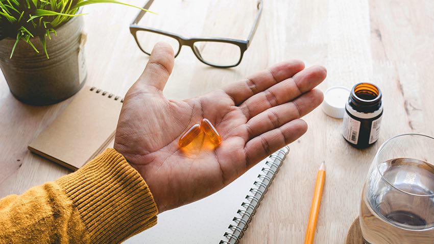 handing holding two pills with eyeglasses in the back