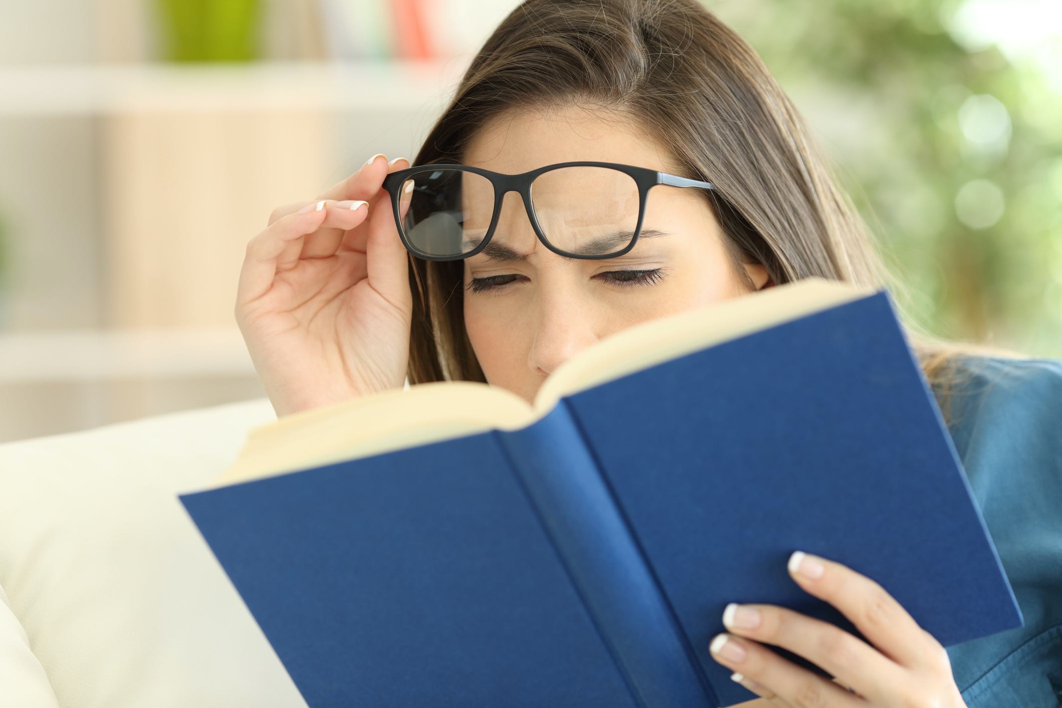 lady who is reading a book and having trouble ready while lifting her glasses to see clearer