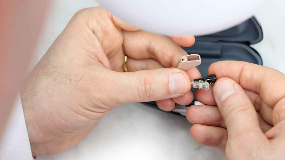 Man works to repair small hearing aid with his hands