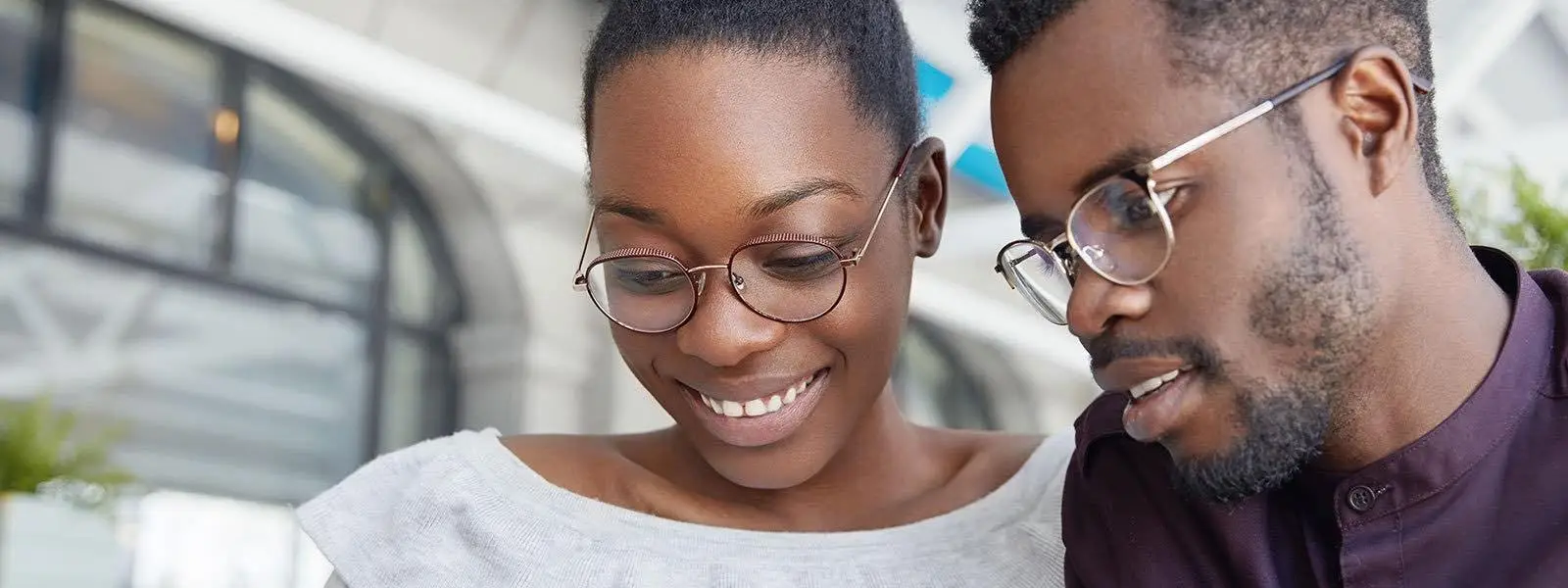 young couple both wearing glasses looking down and smiling
