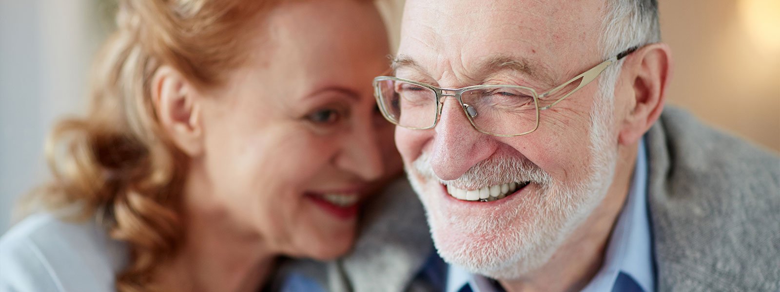 older couple smiling with the woman leaning against the husband