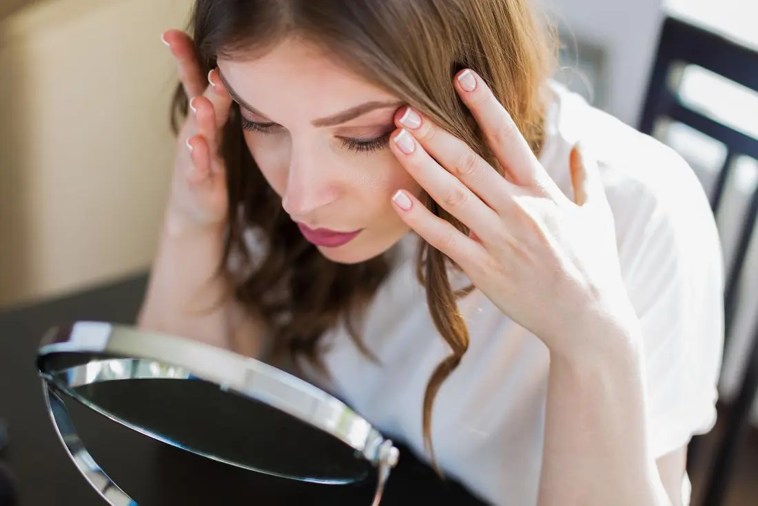 Woman looking stressed into a mirror holding her head in her hands
