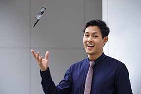 Man wearing a blue shirt and purple tie throwing a pair of black eyeglasses into the air