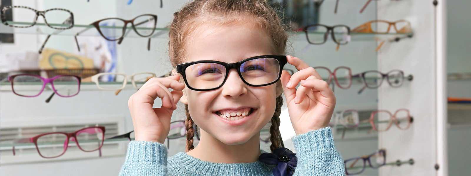 young girl smiling and wearing eyeglasses after an eye exam at an optical shop