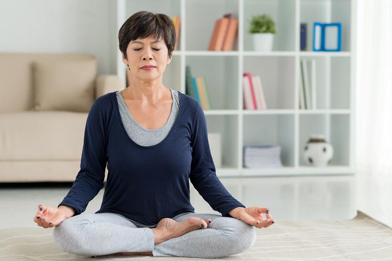 Woman sitting in living room with her eye closed in a meditating position.