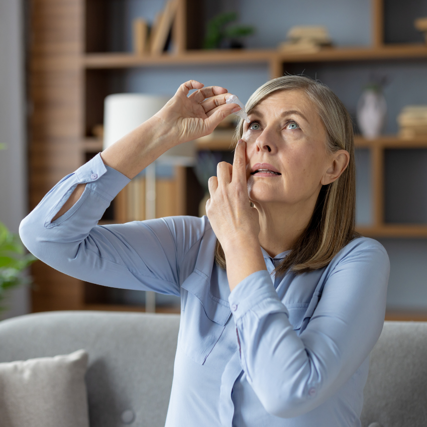 Concentrated mature lady tipping head back and fixing position for applying medical eye drops indoors
