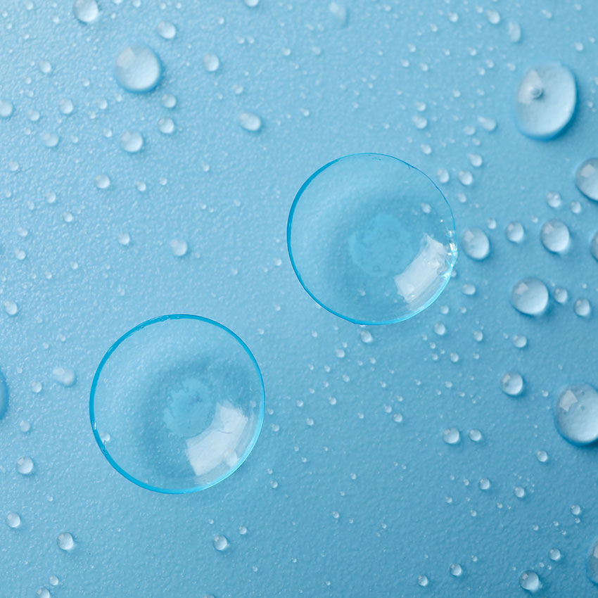 Contact-lenses-on-blue-background-with-water-drops,-top-view
