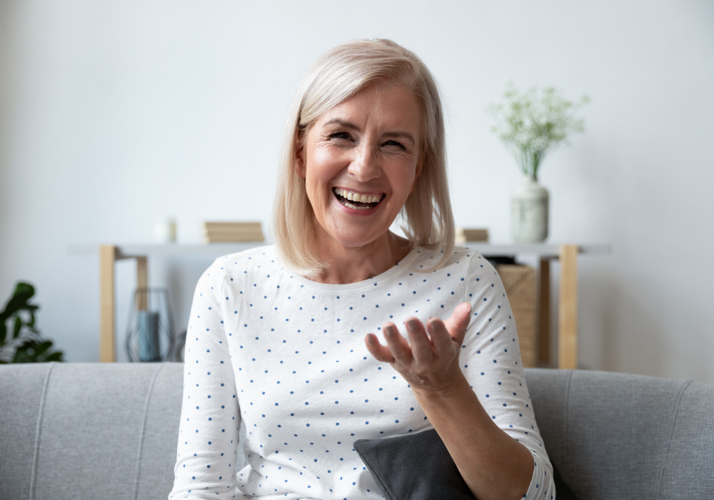 Happy mature blonde lady sitting on couch, holding video call with friends, head shot close up portrait