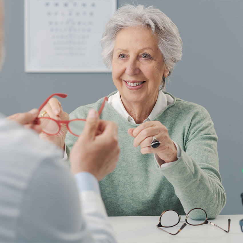 Happy-senior-woman-choosing-her-new-prescription-glasses,-the-eye-care-specialist-is-helping-her