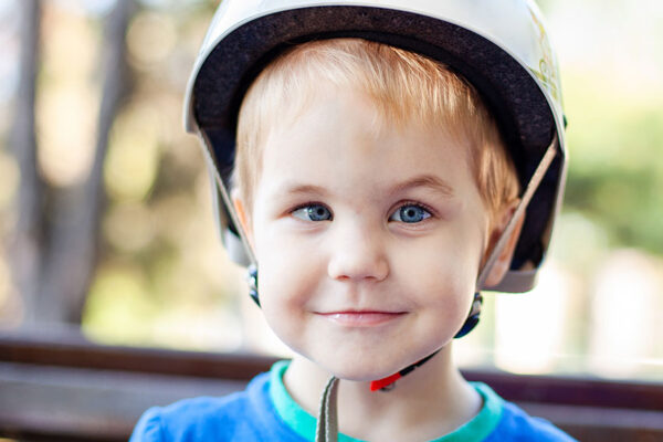 Little-blonde-boy-3-years-old-in-white-sport-helmet-and-blue-t-shirt-outside.-Special-problems-with-kid's-eyes