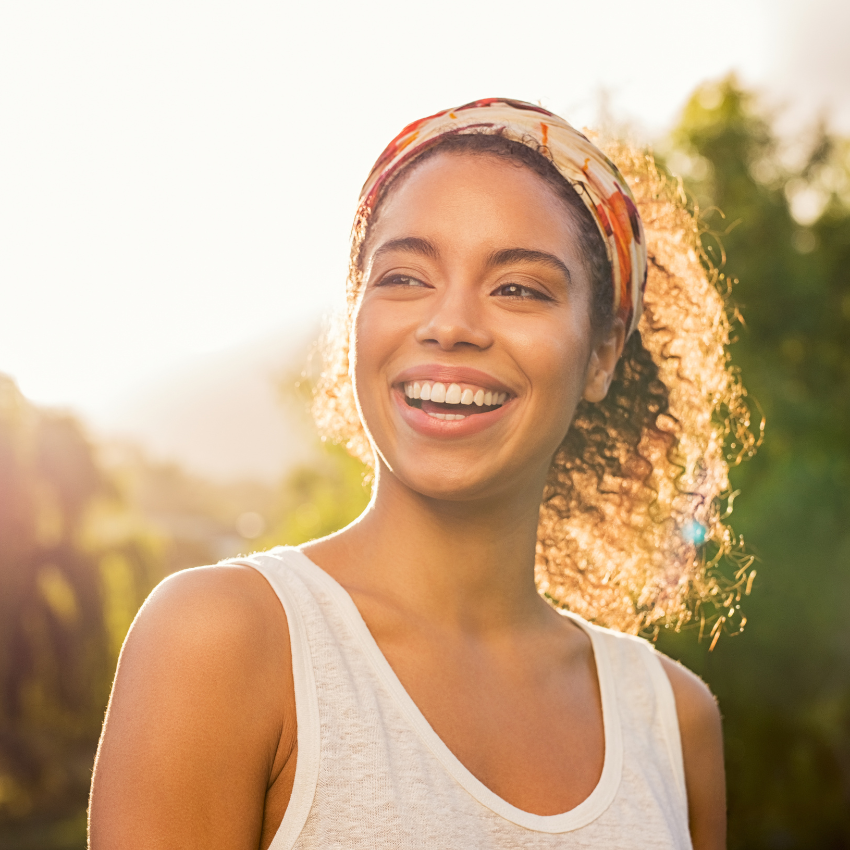 Portrait of african american woman smiling and looking away at park during sunset