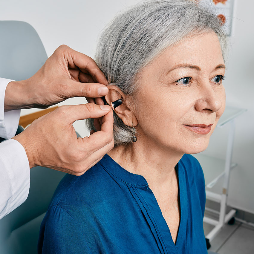 Senior-woman-during-installation-hearing-aid-into-her-ear-by-her-audiologist,-close-up.-Hearing-treatment-for-hearing-impaired-people