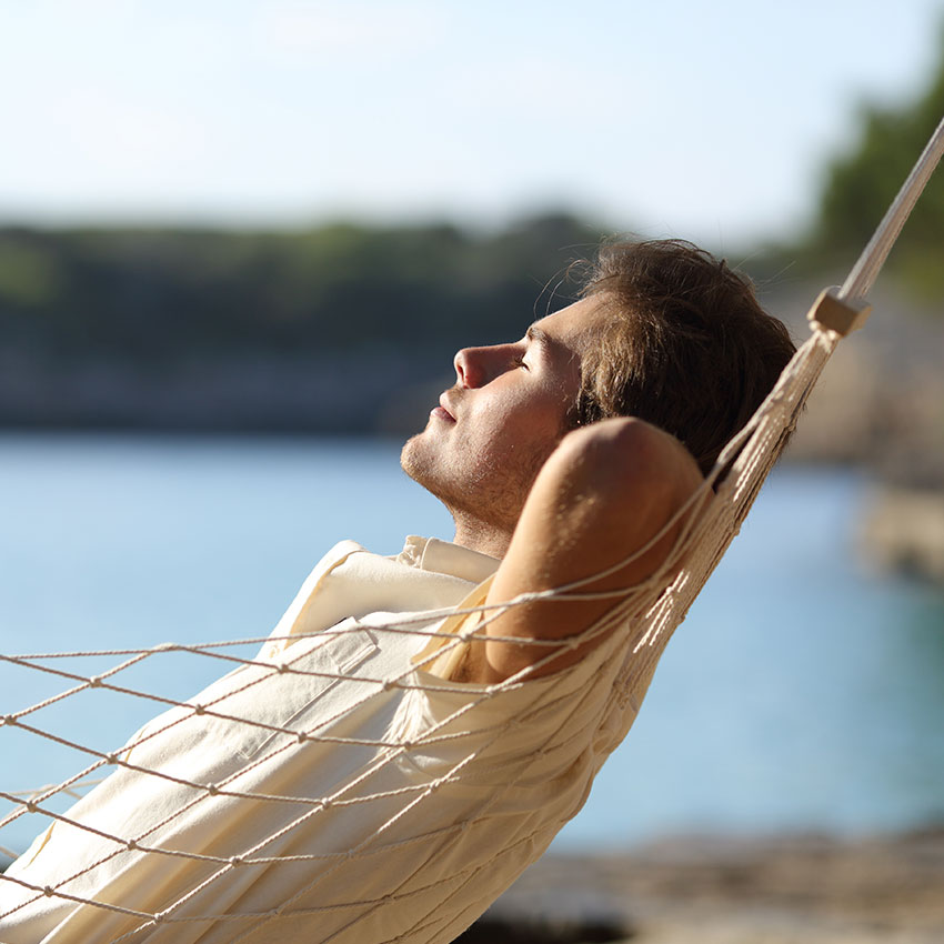 Side-view-of-a-casual-happy-man-relaxing-on-a-hammock-in-the-beach-on-holidays