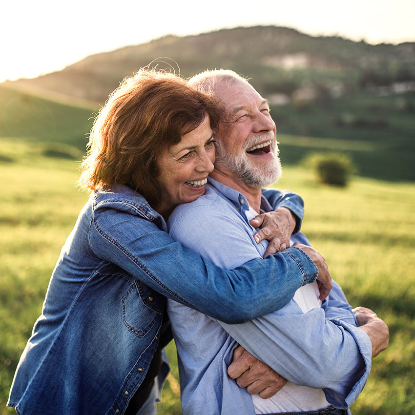 Side-view-of-senior-couple-hugging-outside-in-spring-nature-at-sunset.
