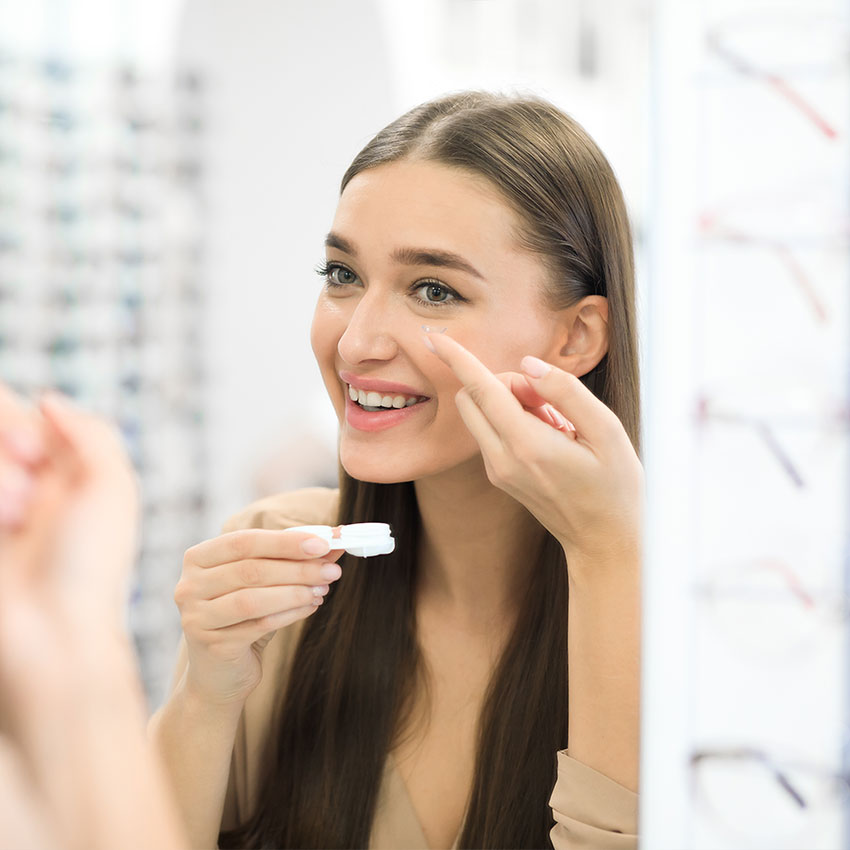 Smiling-woman-holding-contact-eye-lenses-and-container-in-hand,-applying-eye-contacts,-looking-in-mirror