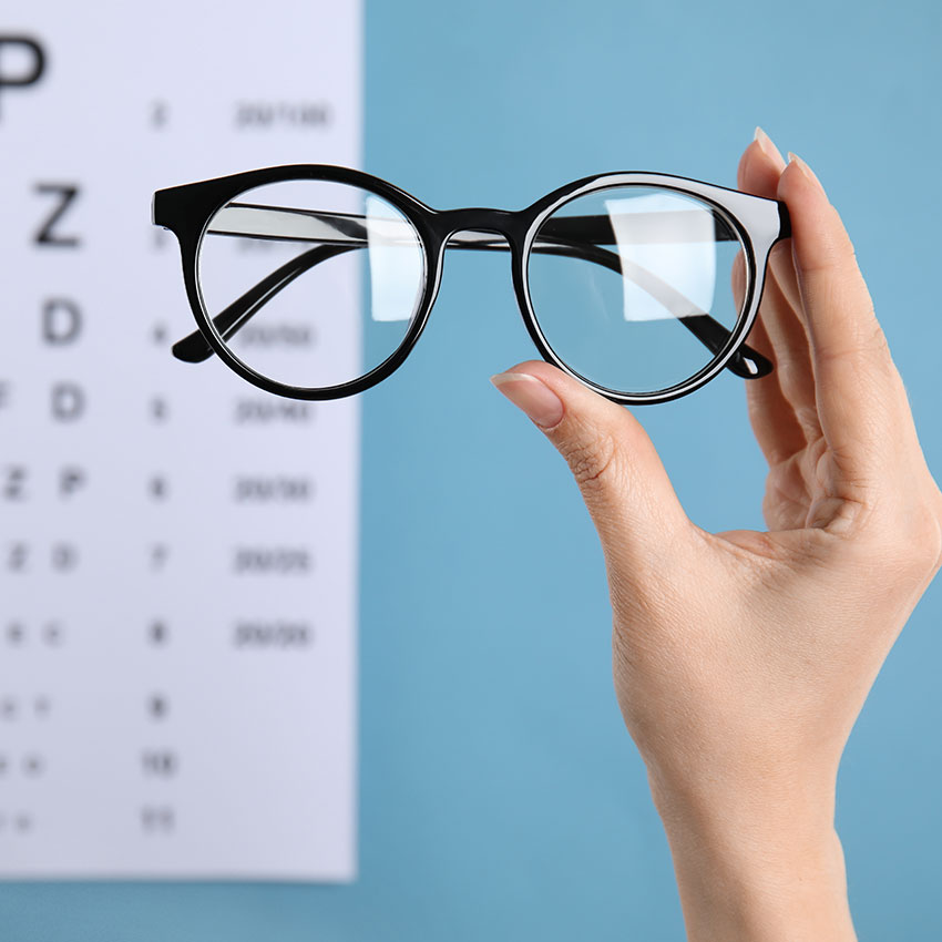 Woman-holding-glasses-against-eye-chart-on-blue-background,-closeup.-Ophthalmologist-prescription