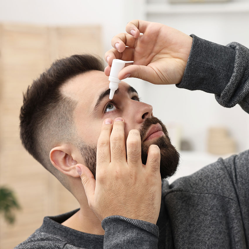 Young-man-applying-medical-eye-drops-indoors,-closeup