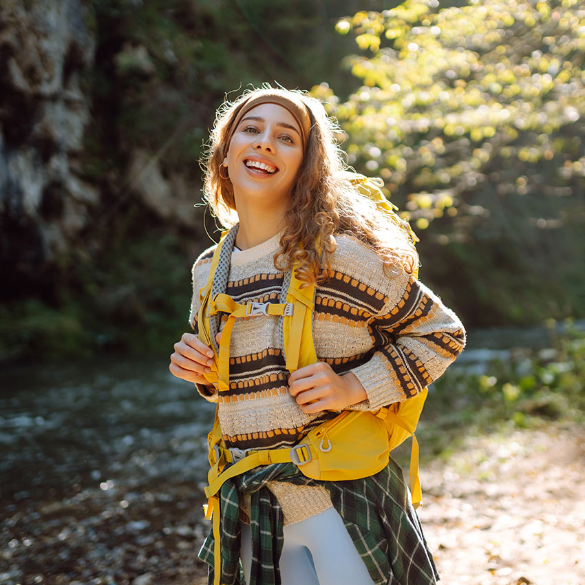 Young woman with colorful backpack enjoying mountain landscape near mountain river