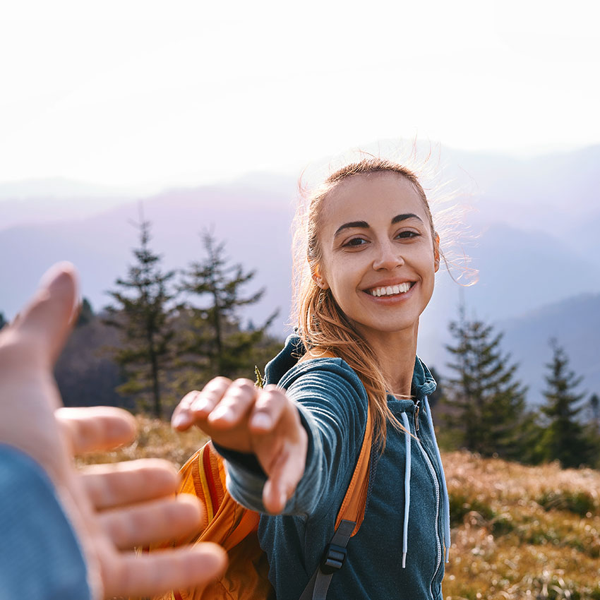 first-person-view-of-a-happy-attractive-woman-hiker-with-backpack-standing-on-edge-of-mountain-ridge-against-background-of-sunset