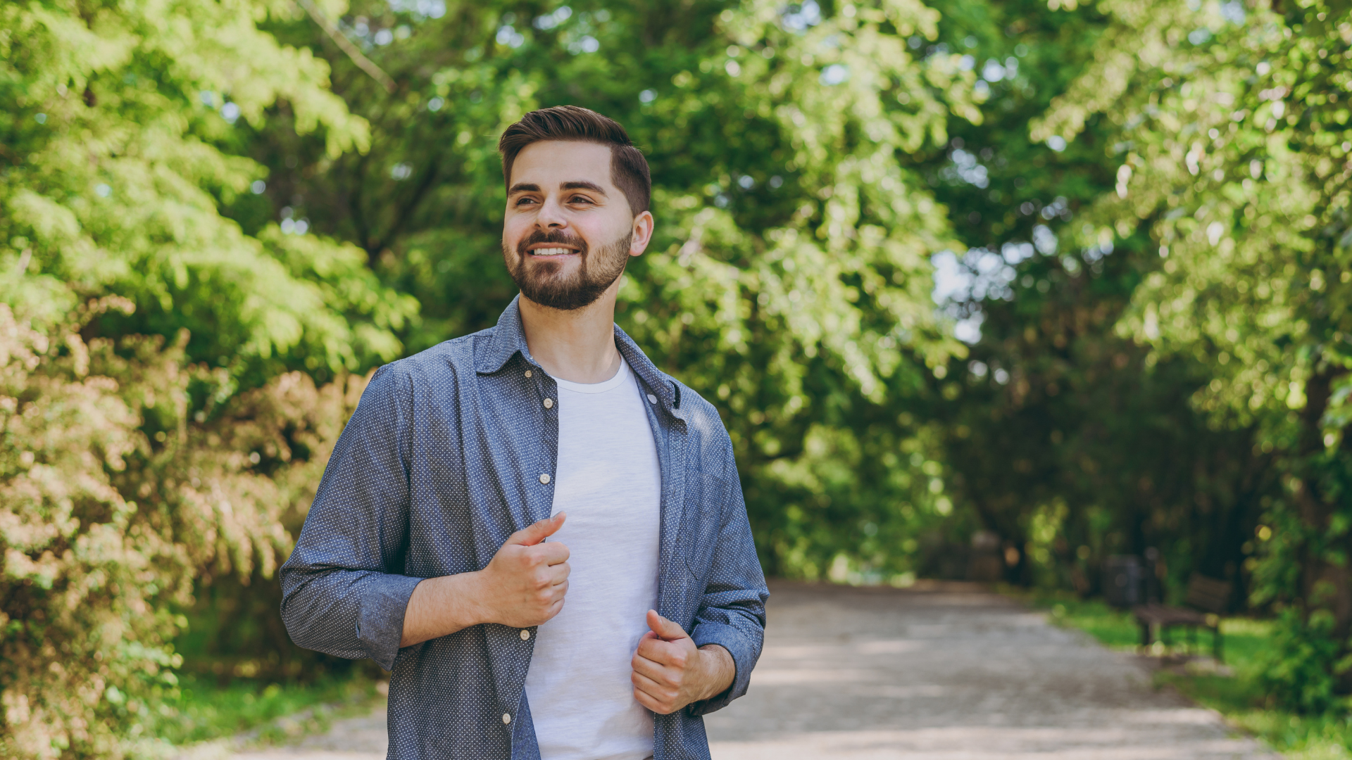 Young minded smiling happy man 20s in blue casual shirt t-shirt walking look aside rest relax in spring green city park