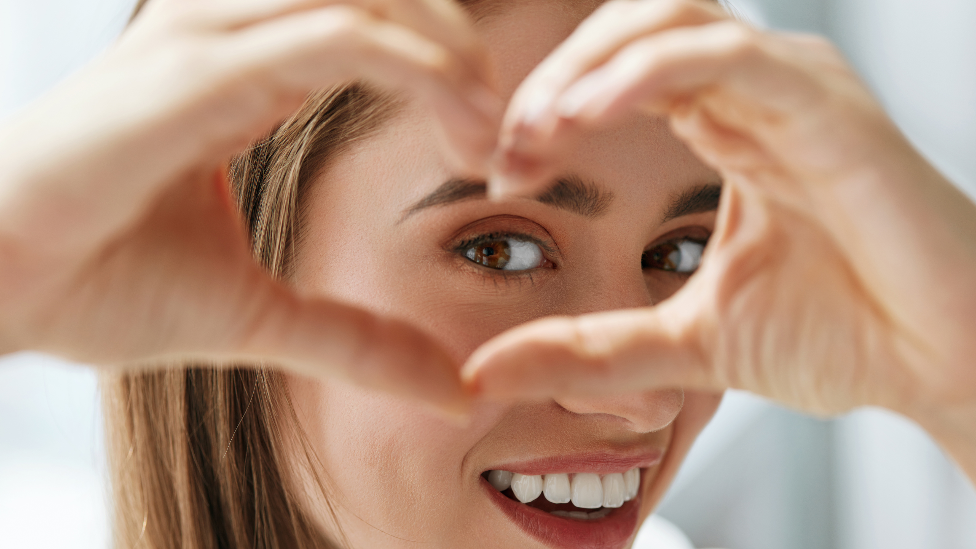 Young woman making heart chape with hands and looking through at camera