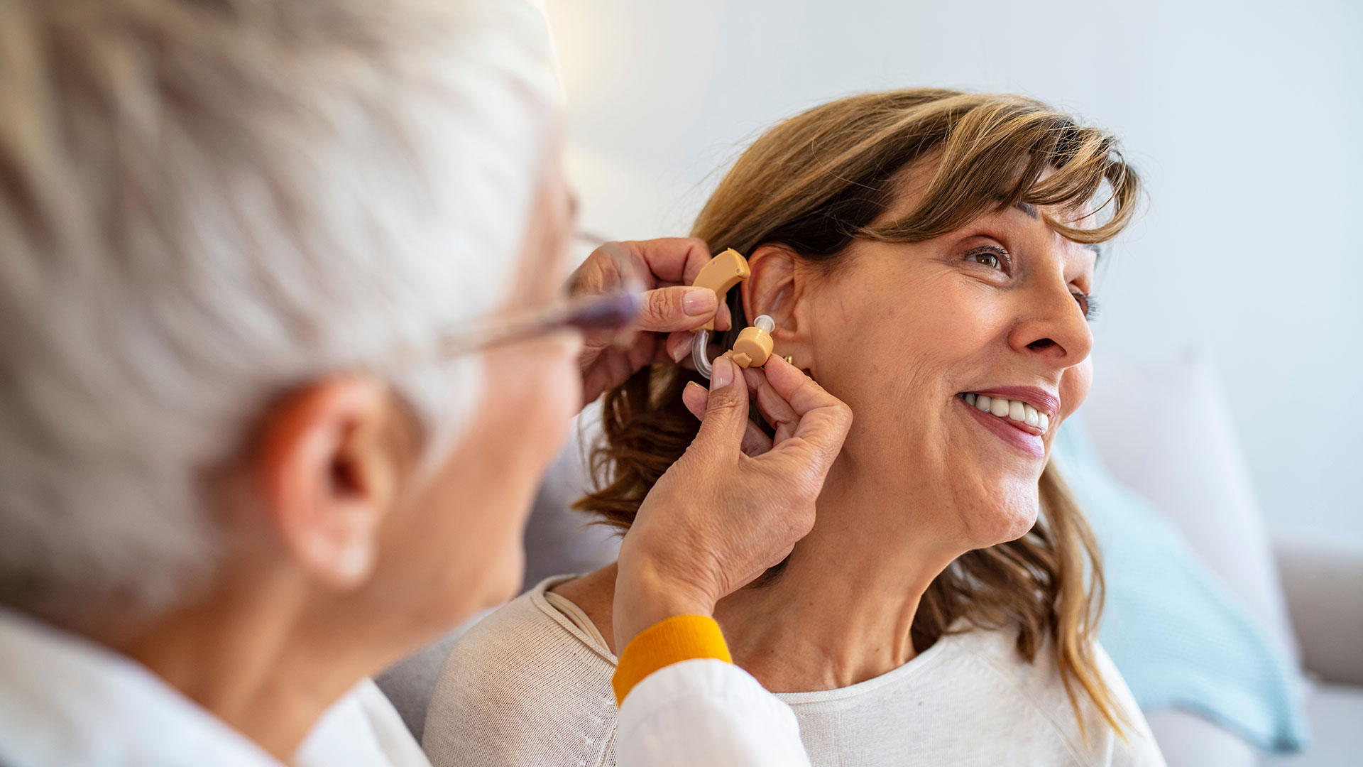 Doctor-helping-senior-patient-with-hearing-aid-,-close-up.-Otolaryngologist-putting-hearing-aid-in-senior