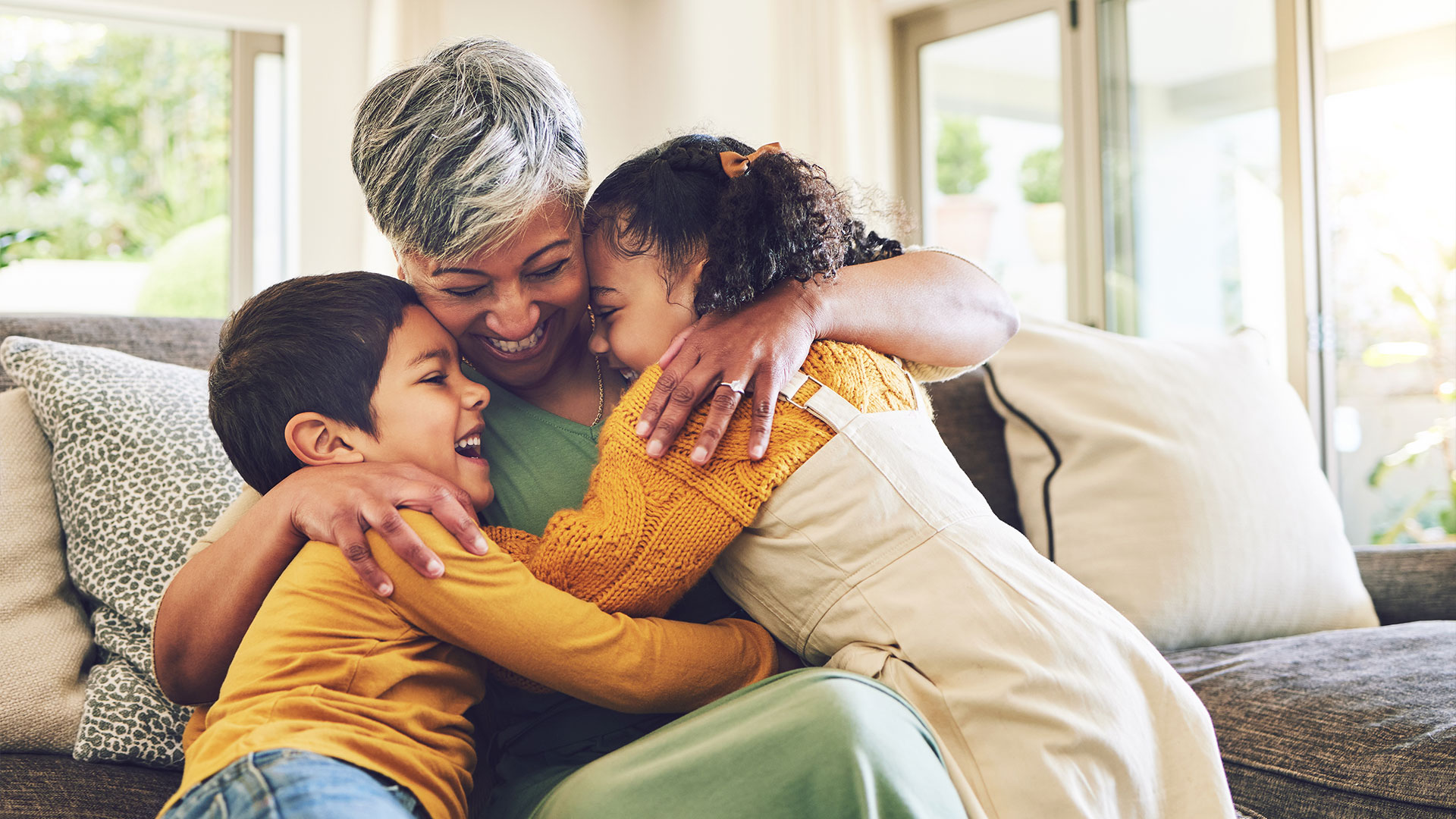 Hug,-grandma-or-happy-kids-on-a-sofa-with-love-enjoying-quality-bonding-time-together-in-family-home