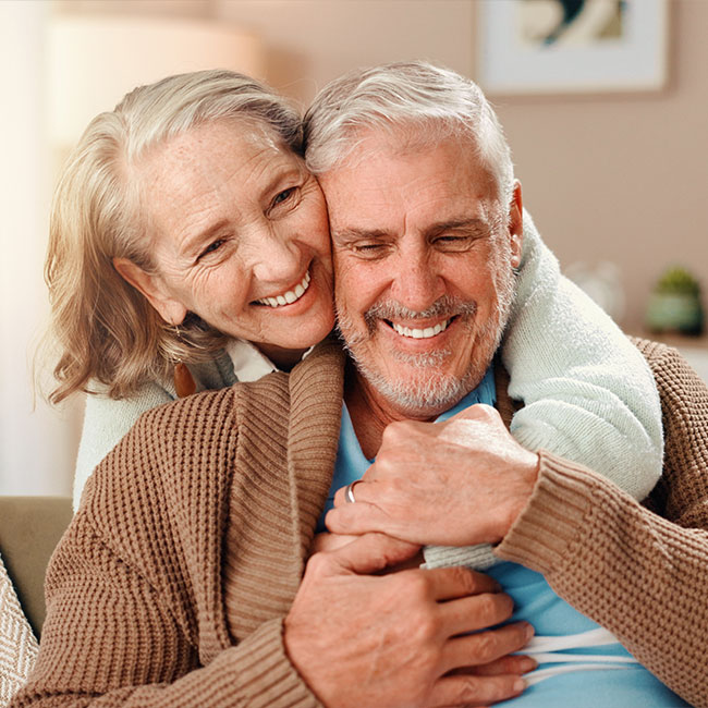 Senior-woman,-man-and-hug-on-sofa-with-smile,-care-and-bonding-with-love-in-retirement-in-lounge