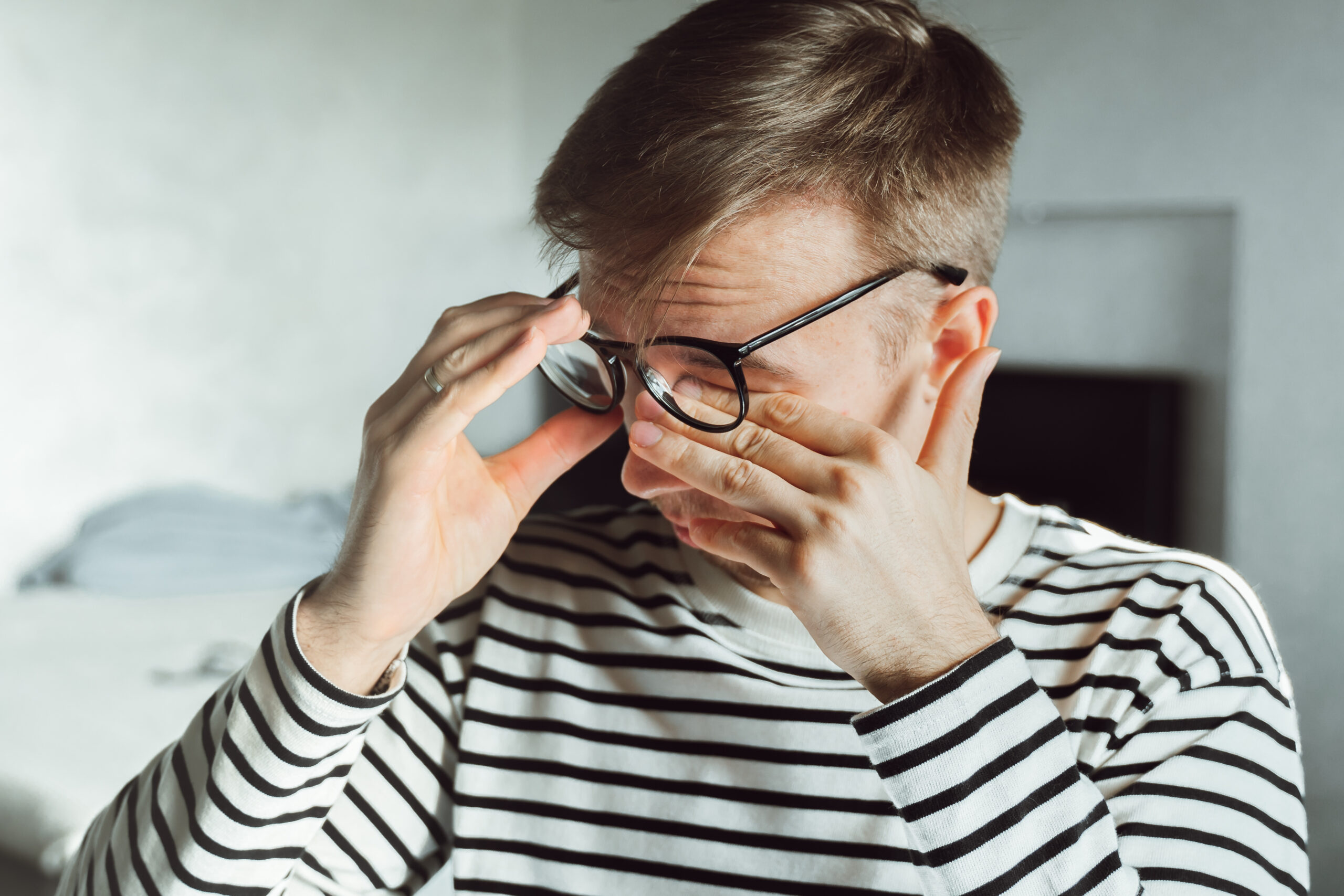 Man taking off glasses and rubbing eye