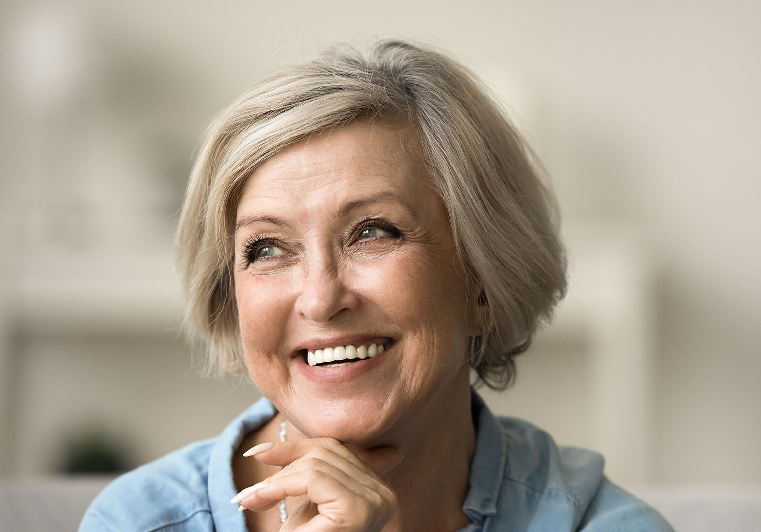 Cheerful-pretty-older-woman-with-trendy-hairstyle-and-white-teeth-touching-chin
