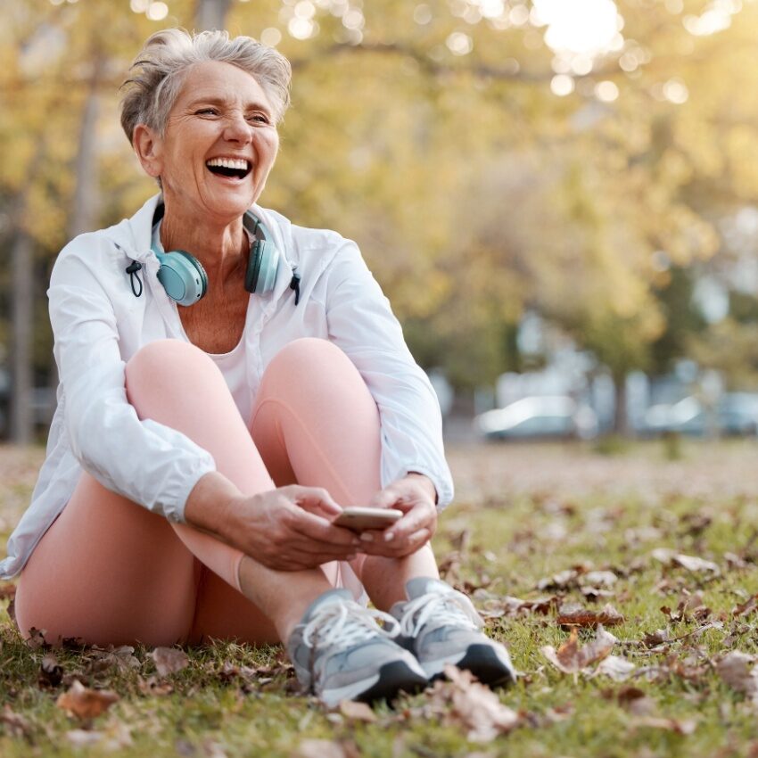 Elderly woman laughing sitting on the grass in a park in active wear