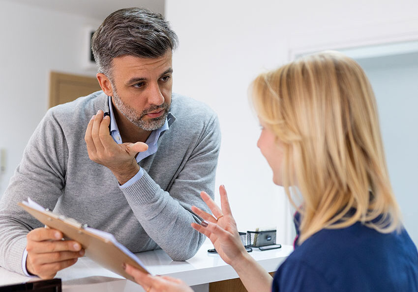 Male-visitor-filling-out-medicine-documents-in-doctor-office.-Patient-asking-about-his-medical-bill.