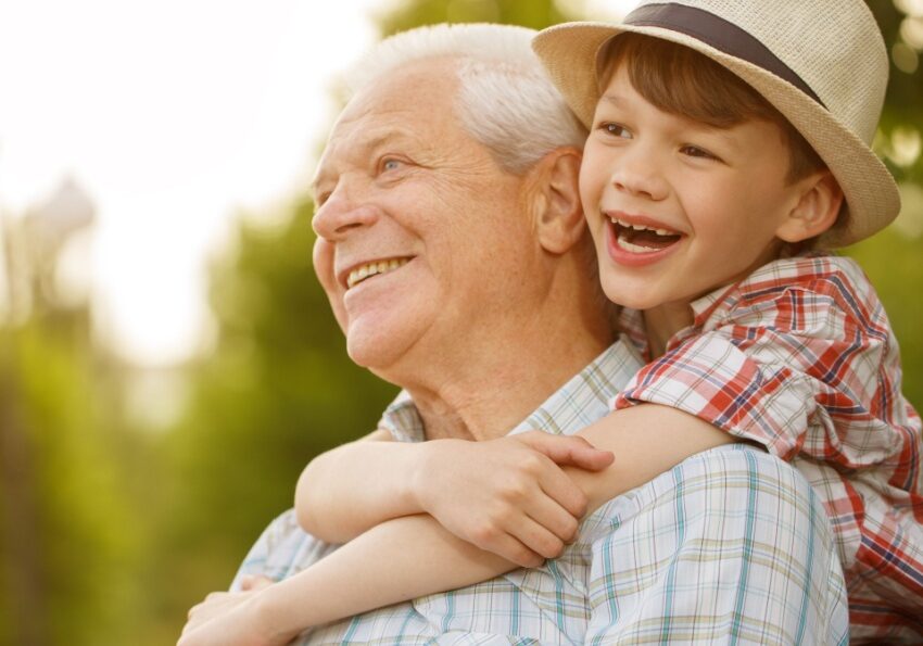 Grandfather and young boy in park with boy hugging him from behind